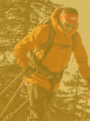 Person skiing downhill wearing an orange jacket, red headband, sunglasses, and carrying a backpack in a snowy forest setting.