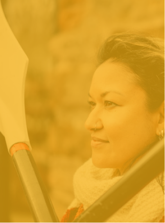 Profile of a woman with earrings and a nose ring, holding a paddle, looking thoughtfully to the side.