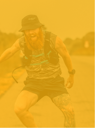 Bearded man wearing a hat, tank top, and shorts running outdoors with a joyful expression.