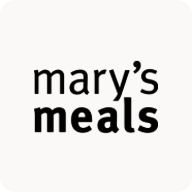 Man with beard in a blue suit and white shirt sitting at a table with clasped hands.