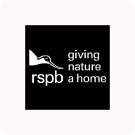 Man with beard in a blue suit and white shirt sitting at a table with clasped hands.