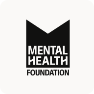 Man with beard in a blue suit and white shirt sitting at a table with clasped hands.