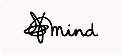 Man with beard in a blue suit and white shirt sitting at a table with clasped hands.