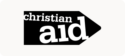 Man with beard in a blue suit and white shirt sitting at a table with clasped hands.