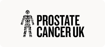 Man with beard in a blue suit and white shirt sitting at a table with clasped hands.