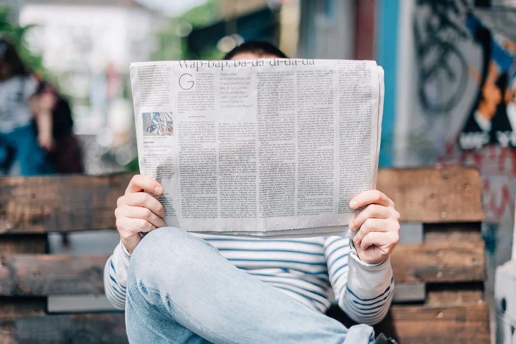A person reading a newspaper on a bench.