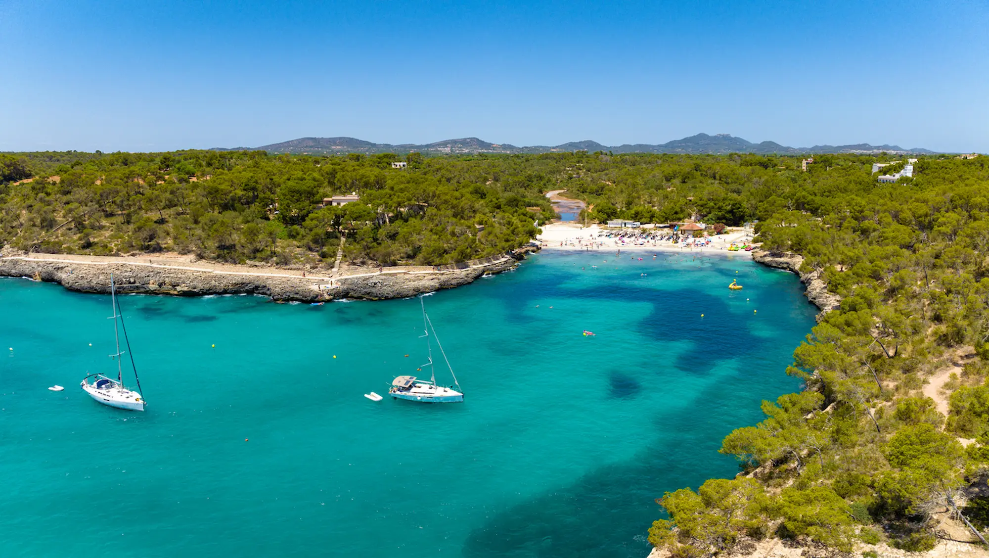 Panoramic of Cala Mondragó cove beach and sail boats in the water