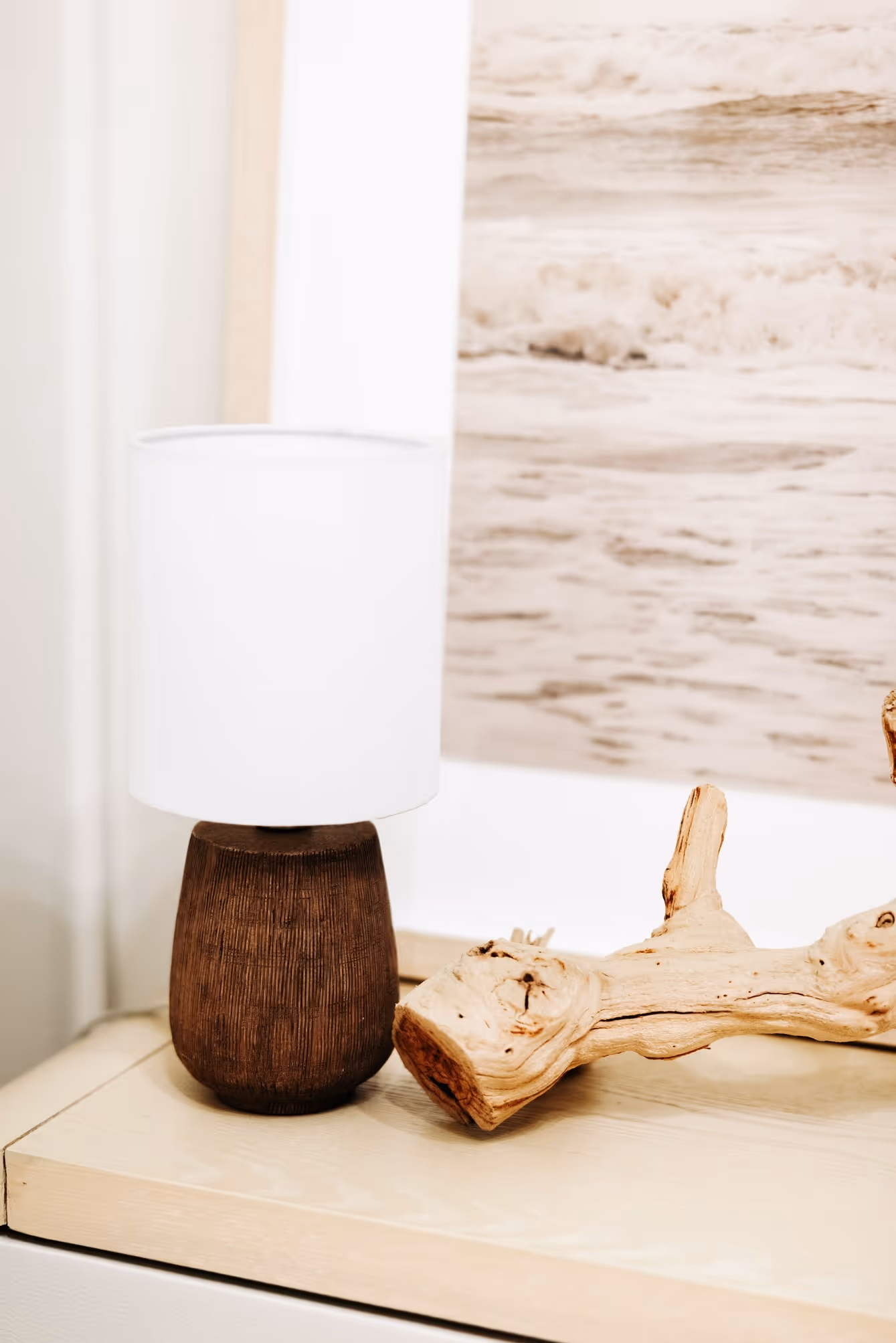 Table lamp with a dark wooden base and white shade next to a piece of driftwood on a light-colored surface.