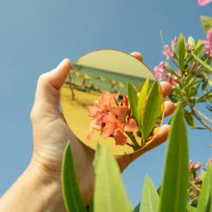 Hand holding a round mirror reflecting pink flowers