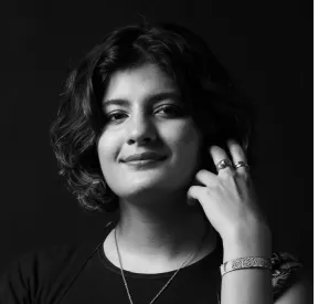 Black and white portrait of a smiling woman with short curly hair, wearing rings, a bracelet, and a necklace.