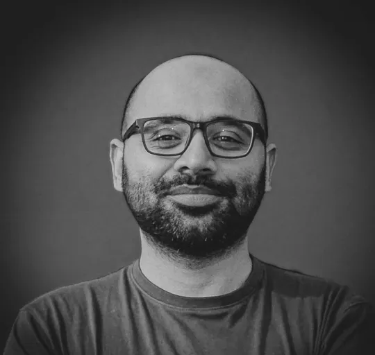 Black and white portrait of a smiling man with glasses and a beard against a plain background.