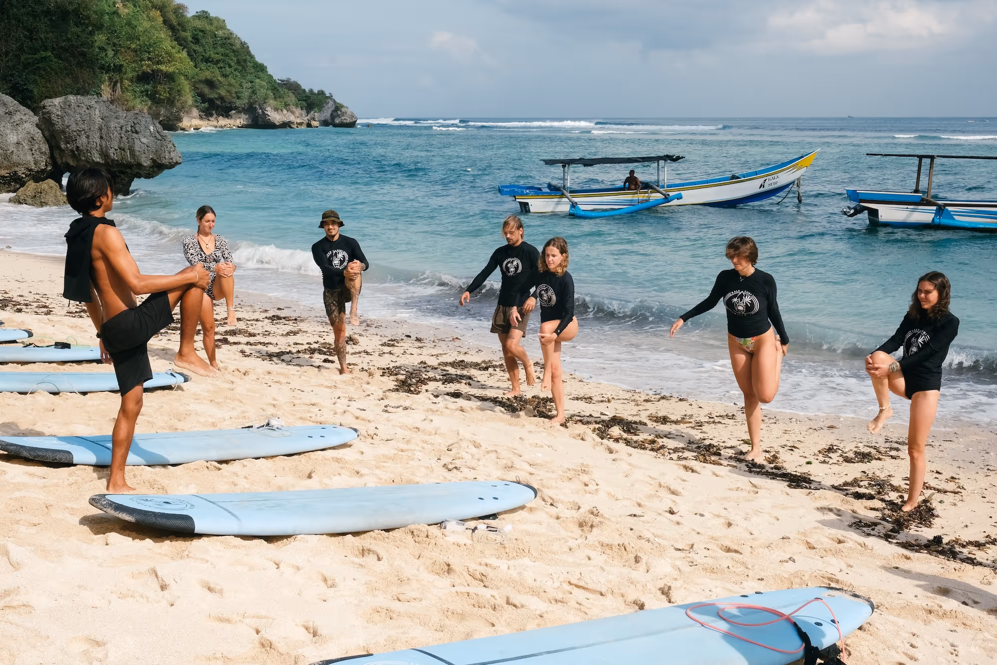 Beginner surf students warming up on the beach with their coach