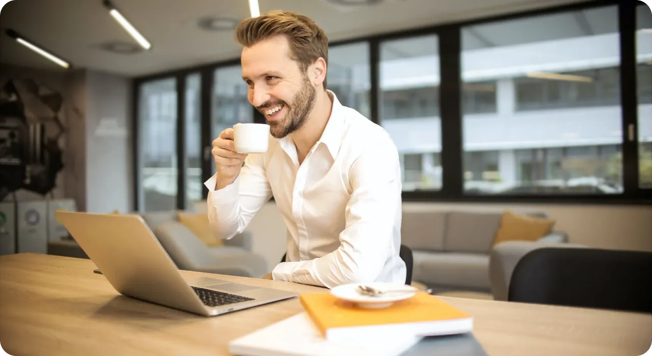 a man sitting at a table with a laptop and a cup of coffee