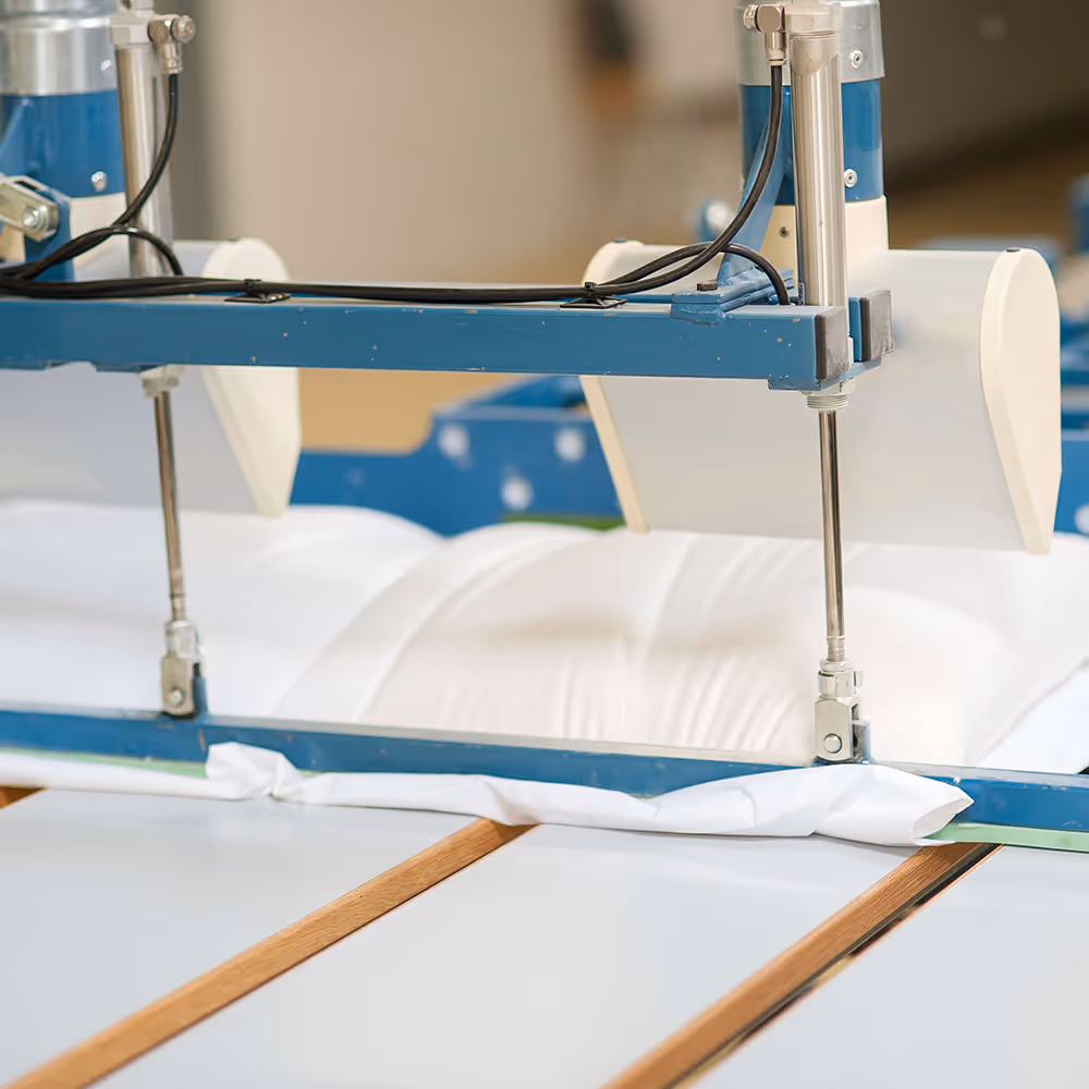 Nahaufnahme einer Maschine, die weißes Stoffmaterial auf einem flachen Tisch spannt.
