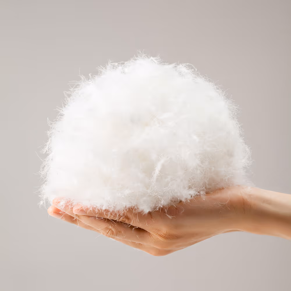 Hand hält eine flauschige weiße Daunenfederwolke vor hellem Hintergrund.