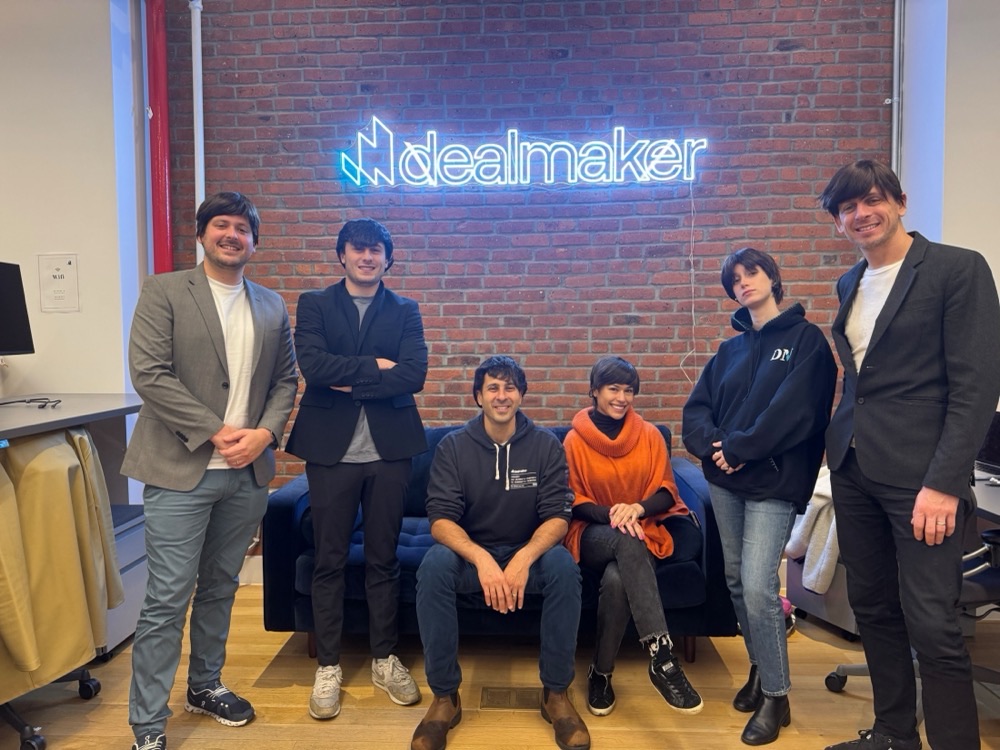 Team members under the DealMaker neon sign