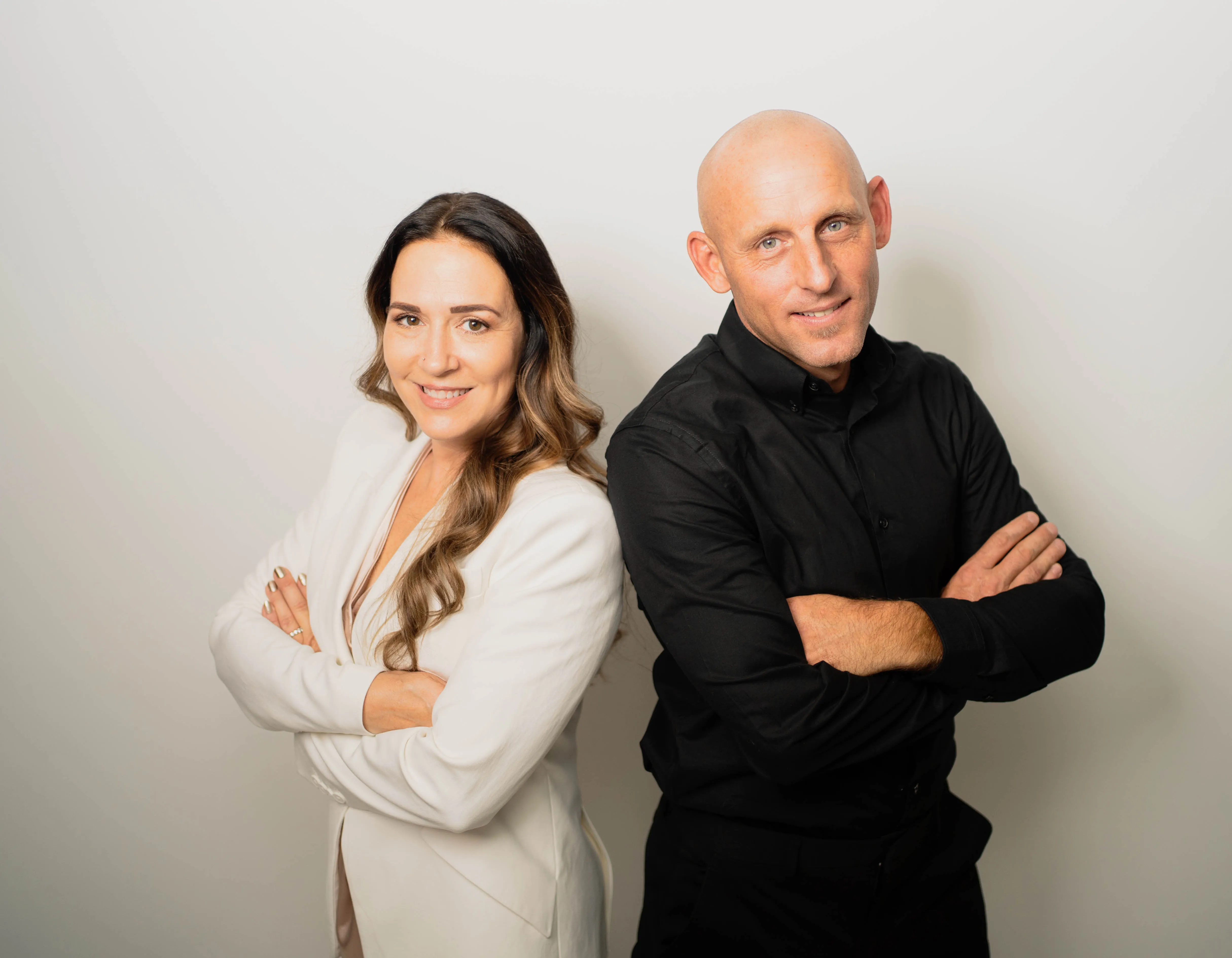 Two business owners standing back-to-back with arms crossed, smiling in professional attire against a neutral studio backdrop.