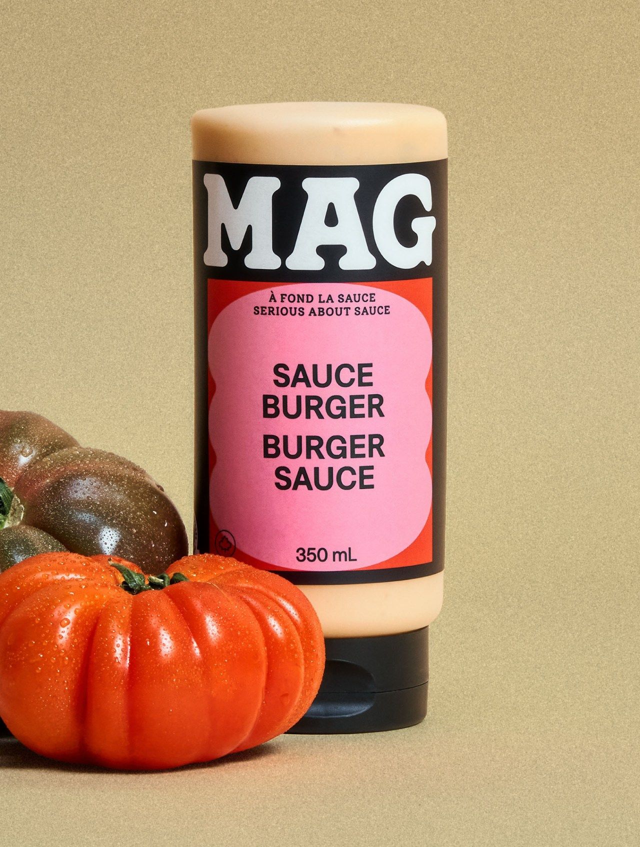 MAG burger sauce bottle with a pink label, styled on tan with heirloom tomatoes