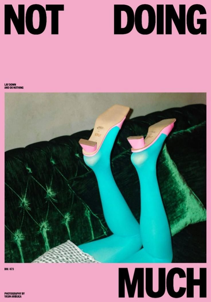 Pink poster reading Not Doing Much with teal-stockinged legs raised against green velvet