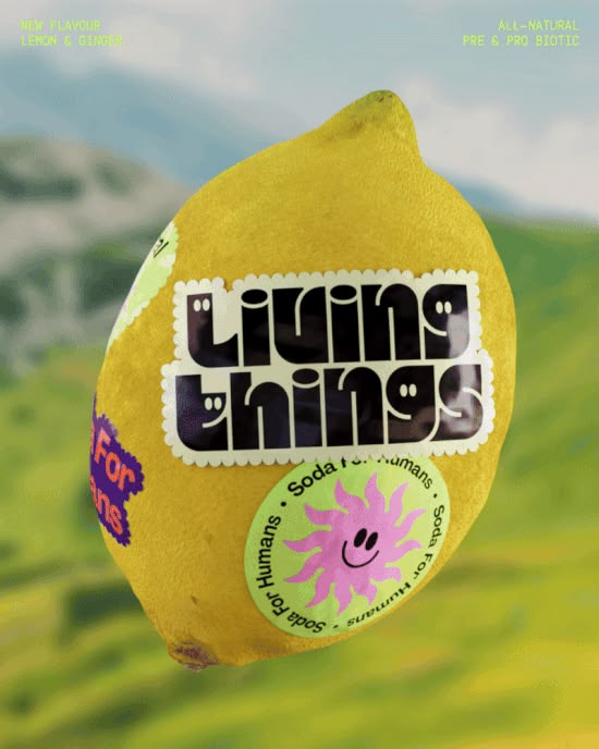 A lemon wrapped in Living Things soda labels and stickers against a green hillside