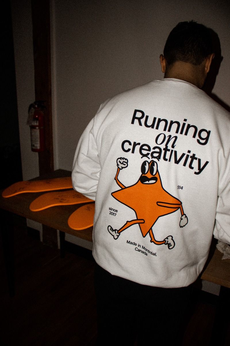 Back of a white sweatshirt reading Running on creativity, with an orange star mascot character below the type