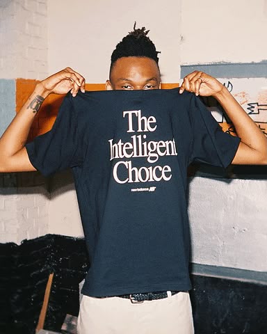 A person holding up a navy New Balance T-shirt printed with The Intelligent Choice in a serif face