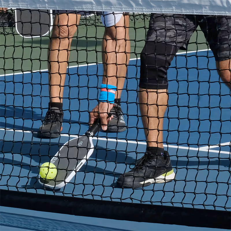 picking up a pickleball in front of the net