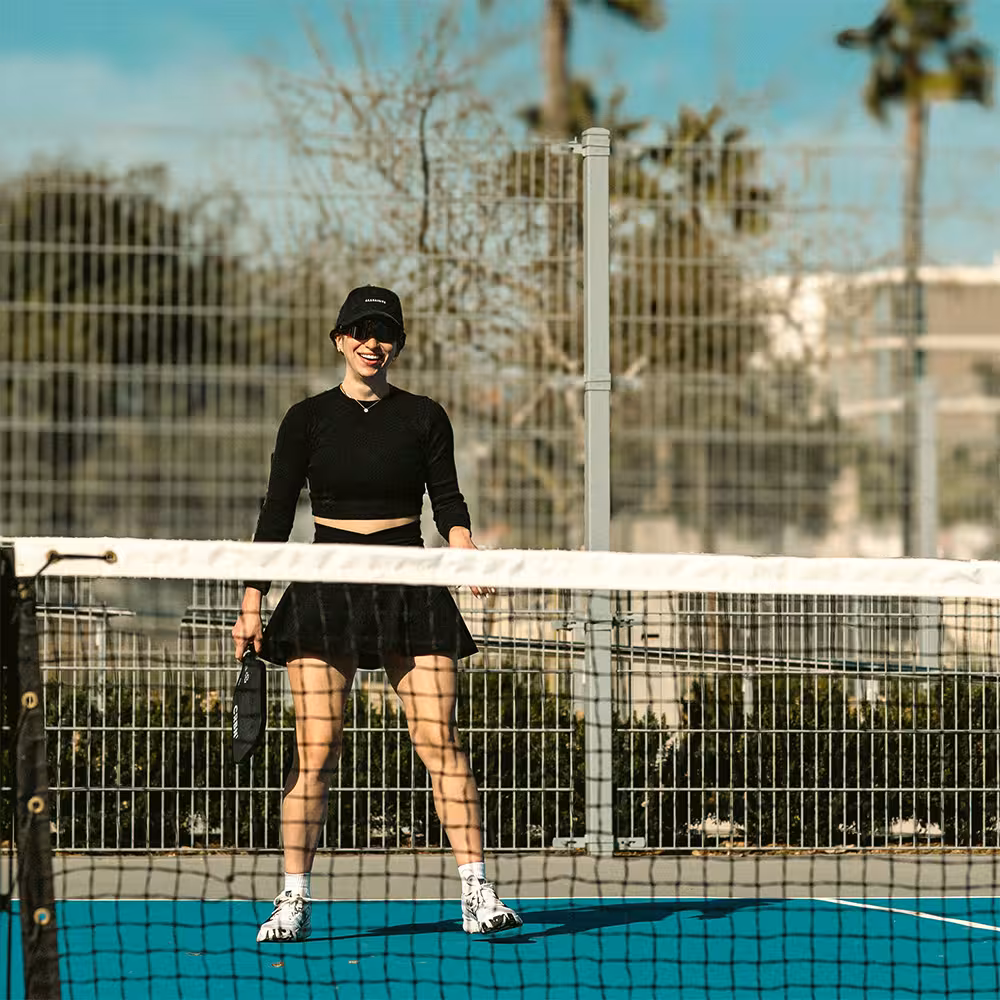 woman in black clothes smiling while playing pickleball