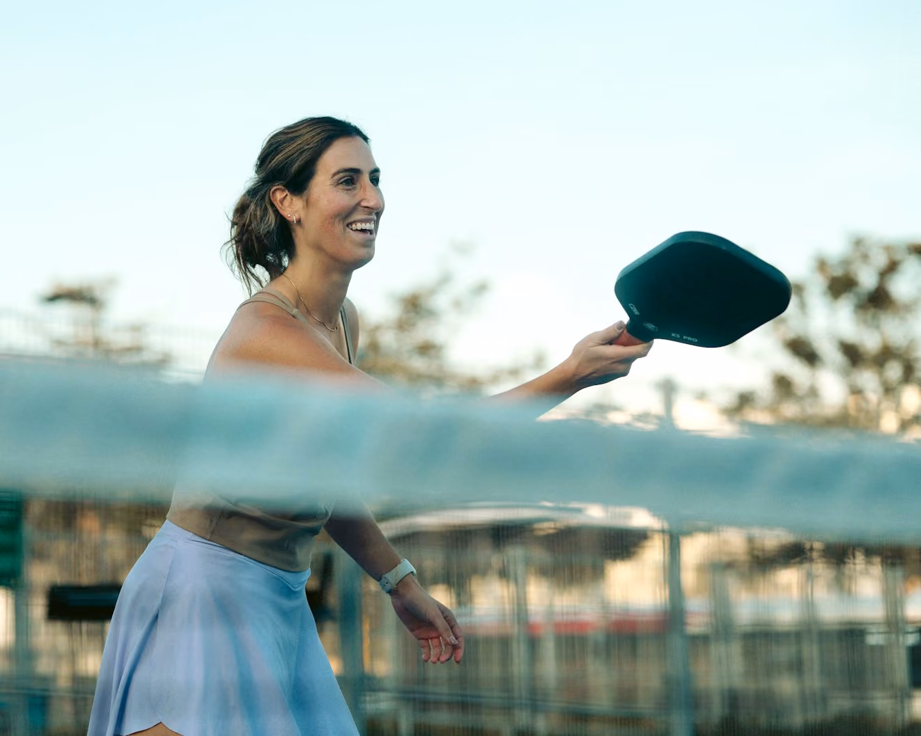 woman smiling hitting a forehand dink at the kitchen on a pickleball court