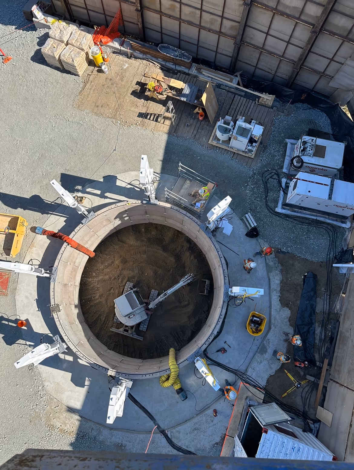 An overhead view of a shaft installation, with an excavator removing soil from the shaft interior.