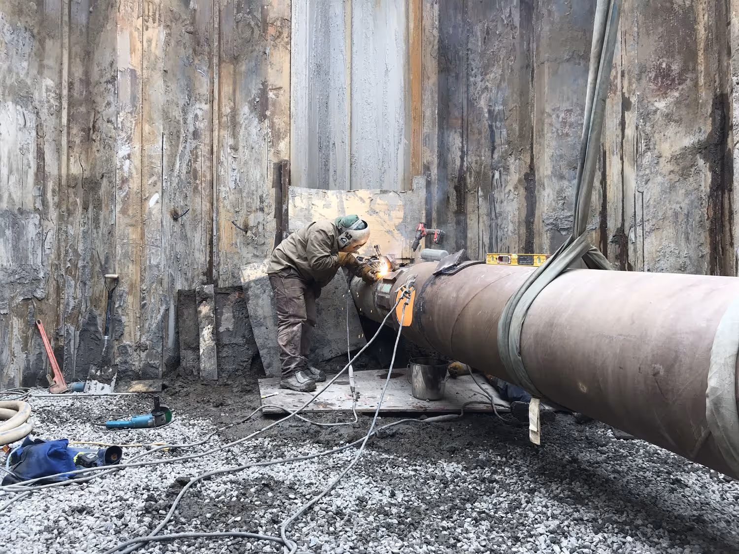 a welder works on a pipe in a pit