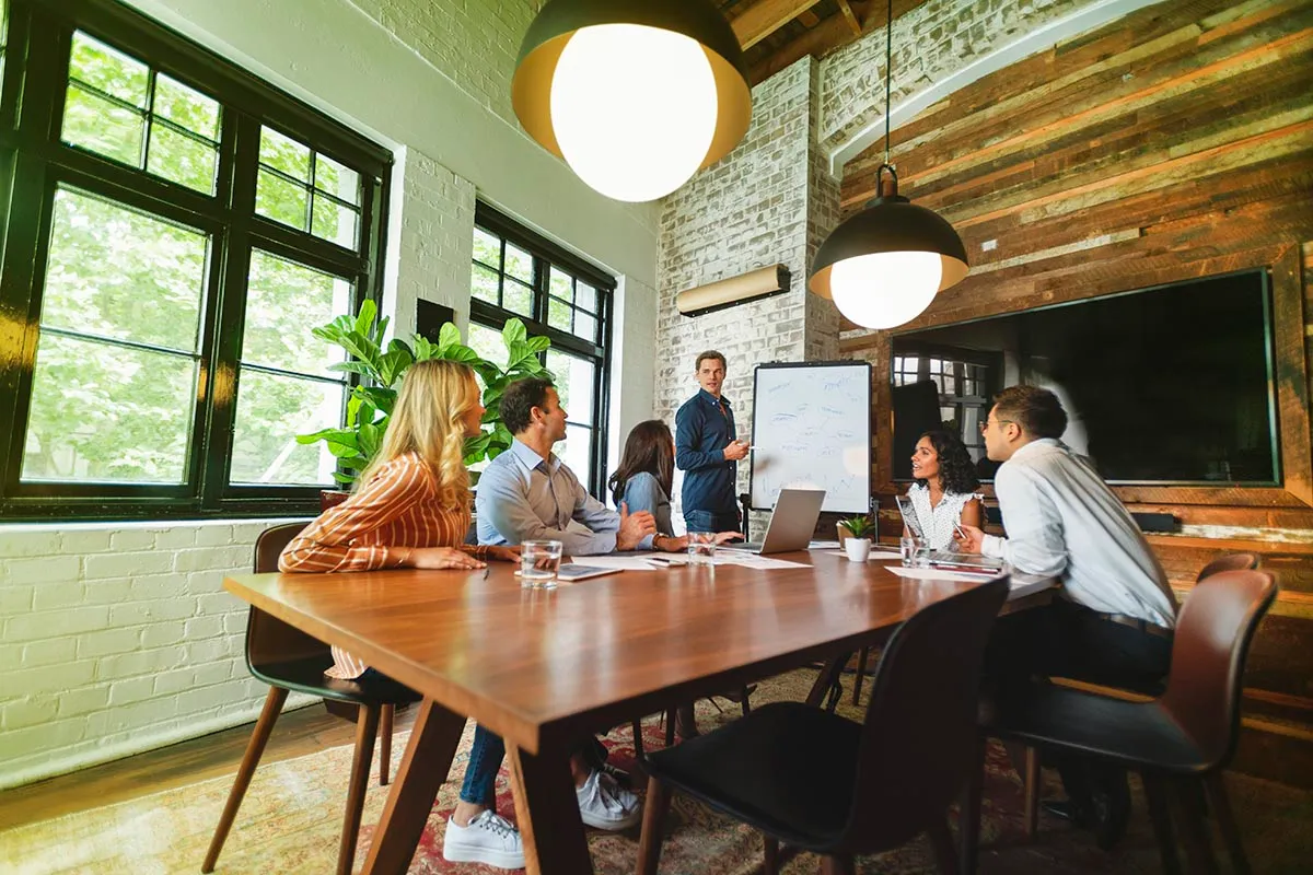 Mensen aan een tafel die samen overleggen en kijken naar een man bij een whiteboard