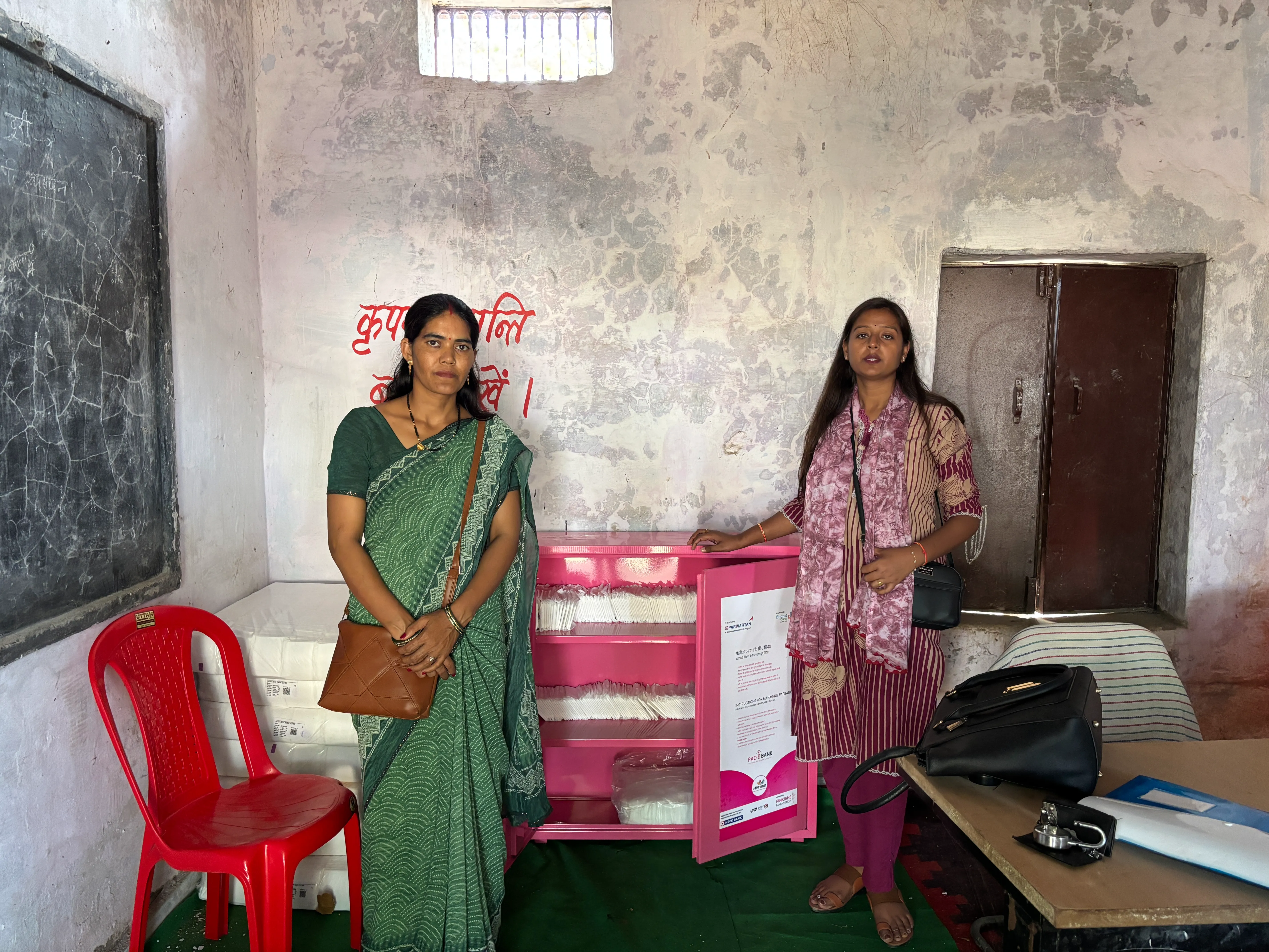 Two women beside a stocked Pinkishe sanitary pad vending cabinet in a school