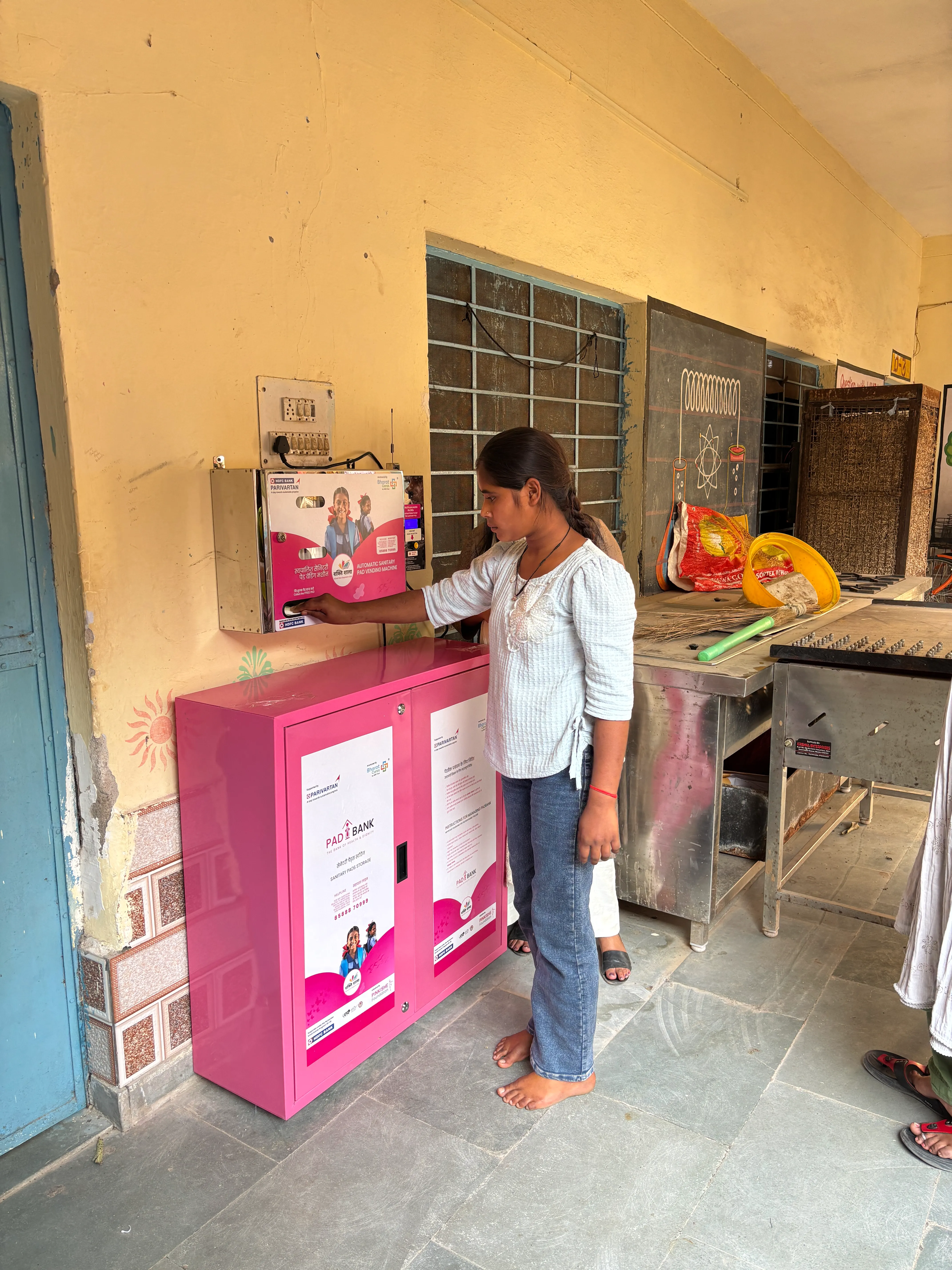 A schoolgirl taking a sanitary pad from a pink Pinkishe vending cabinet