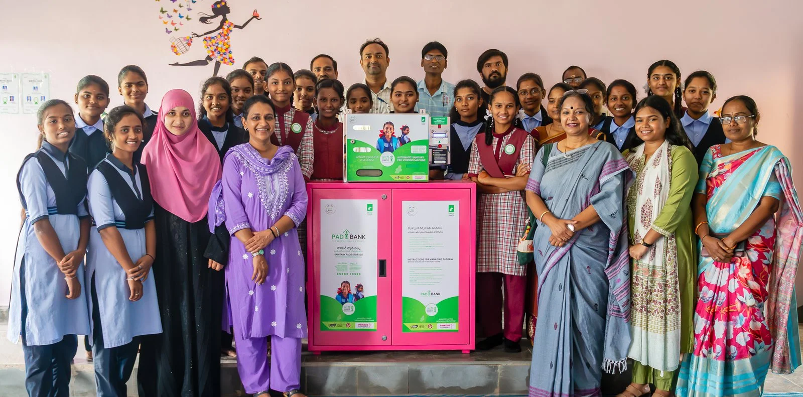 Teachers and students standing with a sanitary pad dispensing machine and Pad Bank at a government school in Adilabad district, Telangana