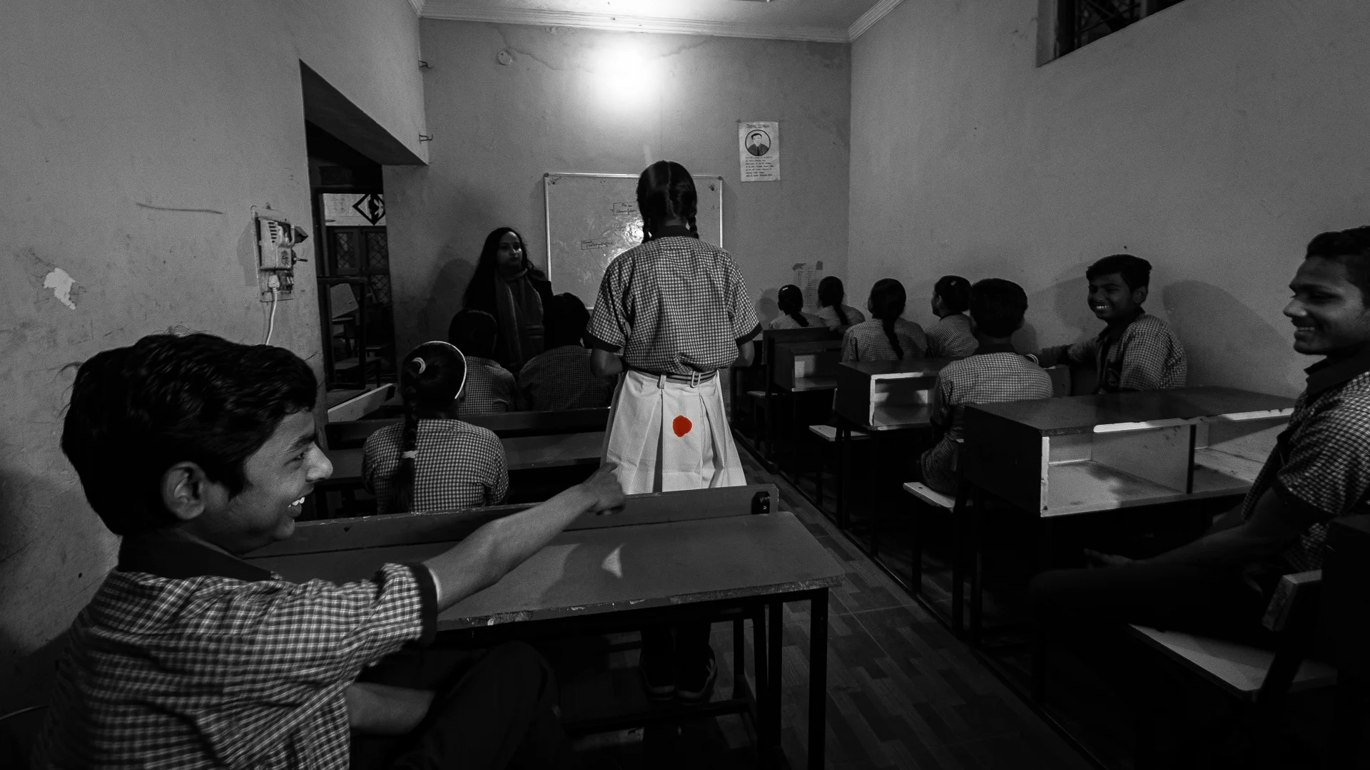 A schoolgirl standing in class with a stain on her uniform while classmates look on