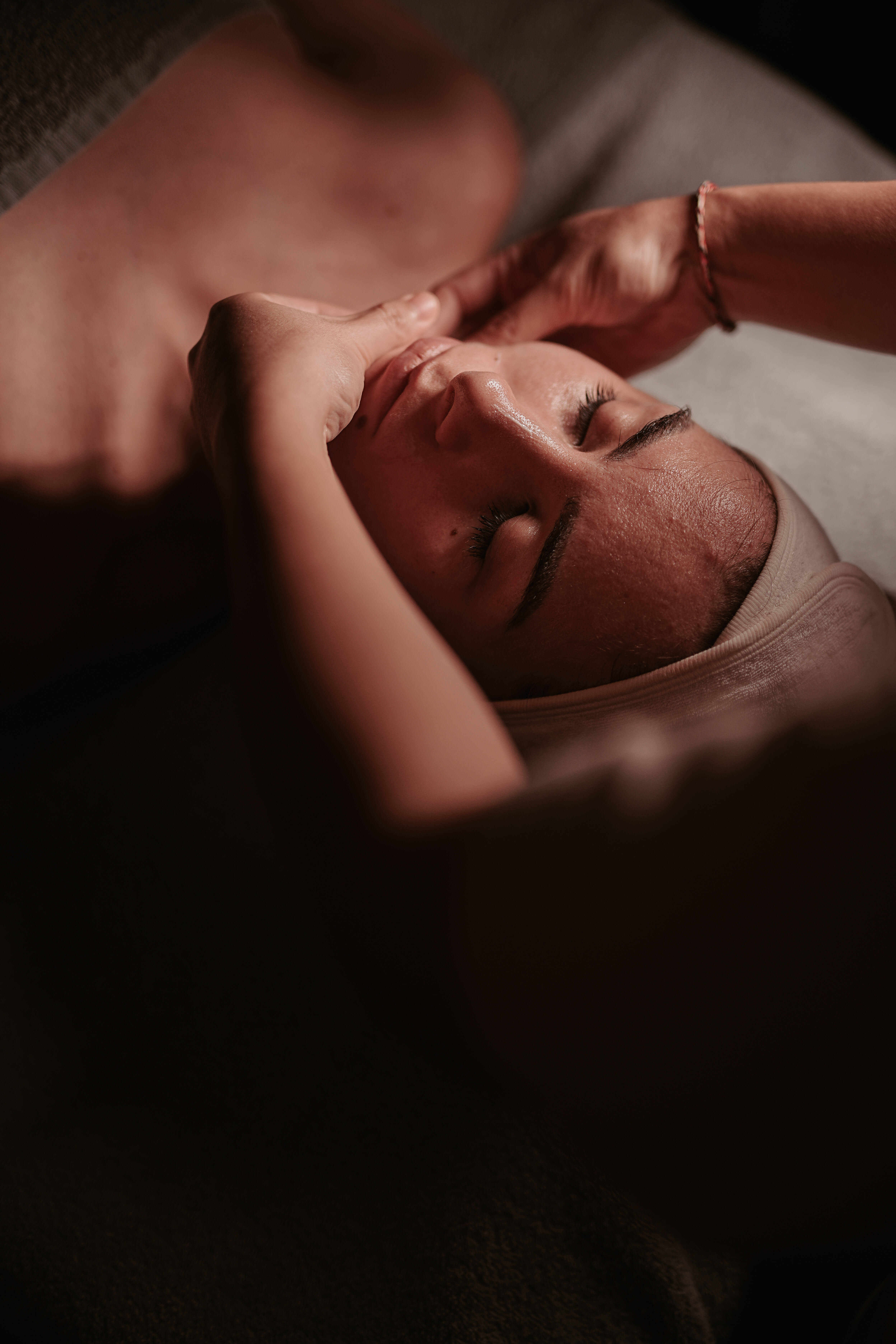 Woman receiving a relaxing facial massage with closed eyes and headband in a dimly lit spa setting.