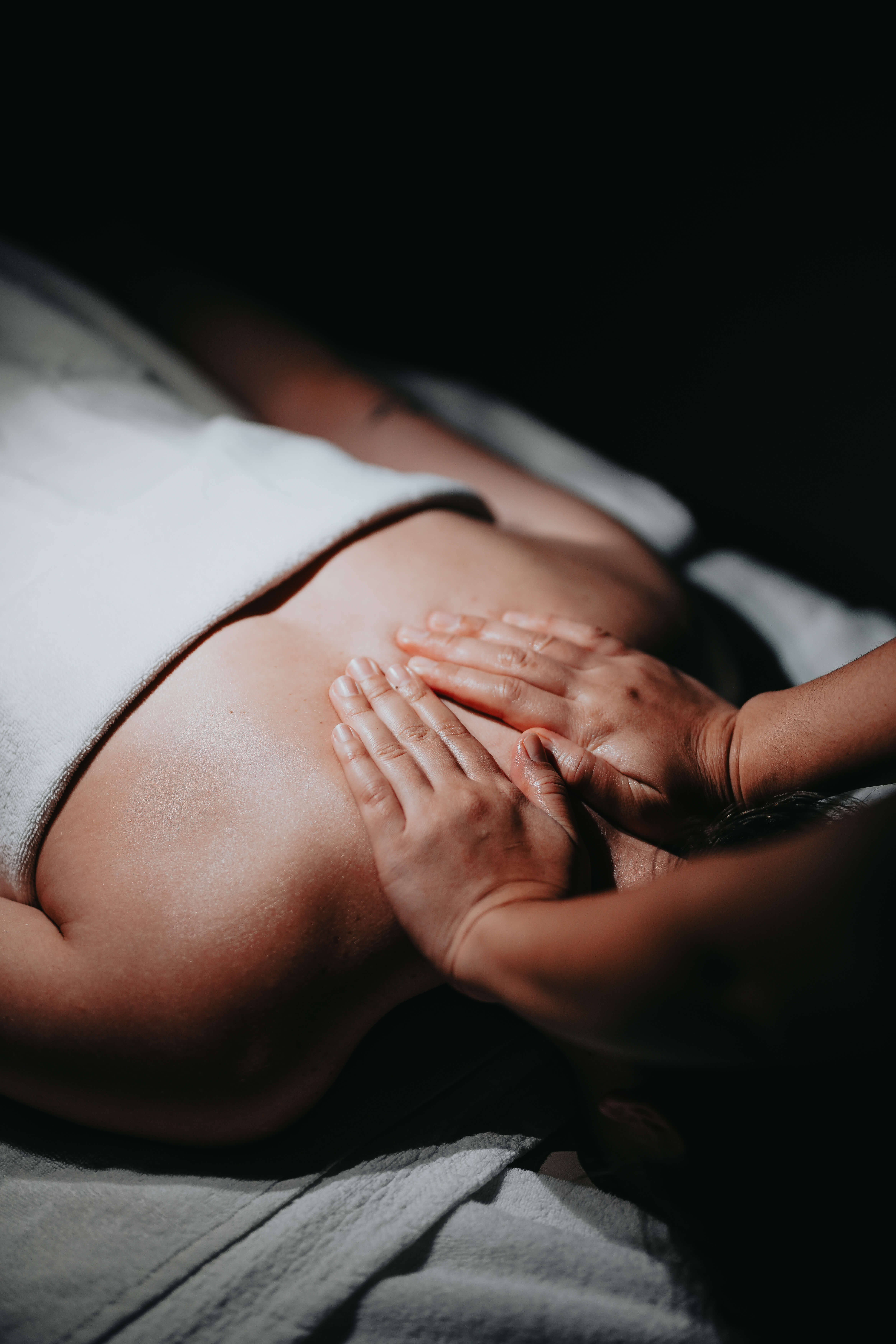 Person receiving a back massage with hands pressing on upper back, lying on a white towel.