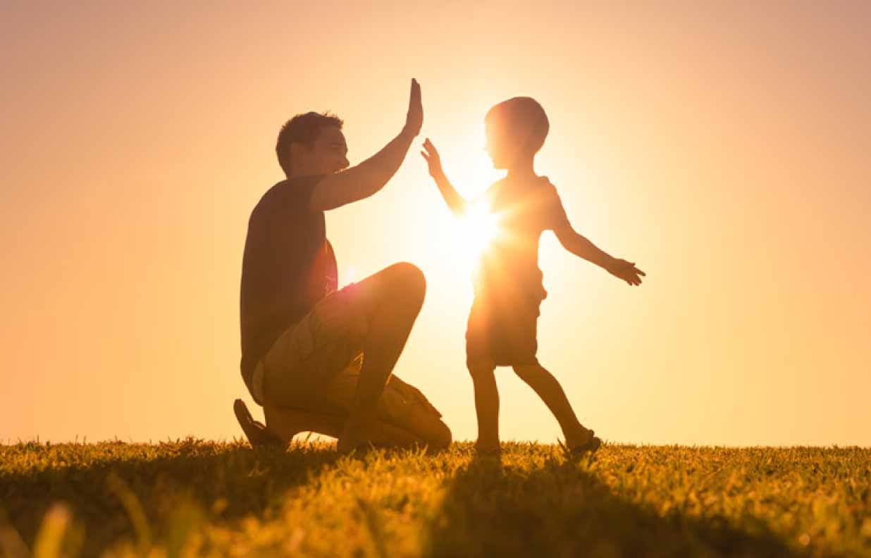 Vater und Kinder schlagen vor einem Sonnenuntergang auf einer Grasflaeche ein