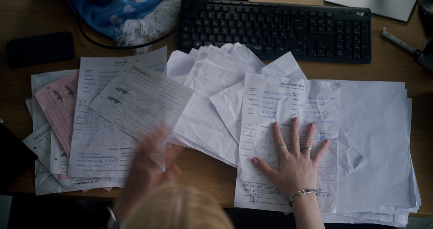 Hände sortieren mehrere Palettenscheine auf einem Schreibtisch vor einer Computer-Tastatur.