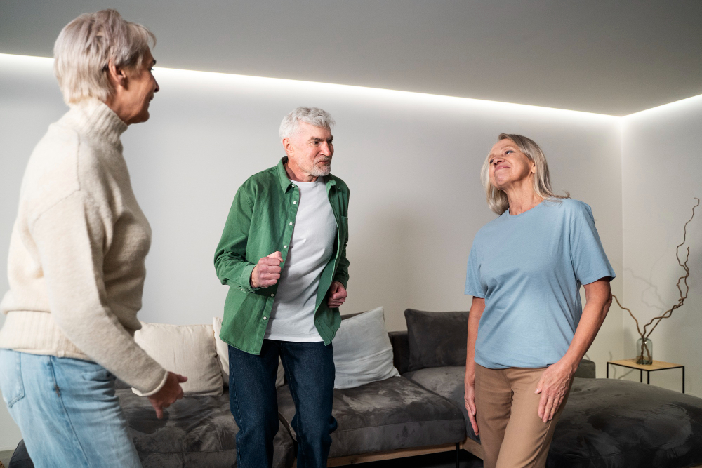 Trois personnes âgées actives qui échangent dans un salon moderne et confortable, illustrant l'autonomie et le bien-être à domicile favorisés par l'aide au logement senior.