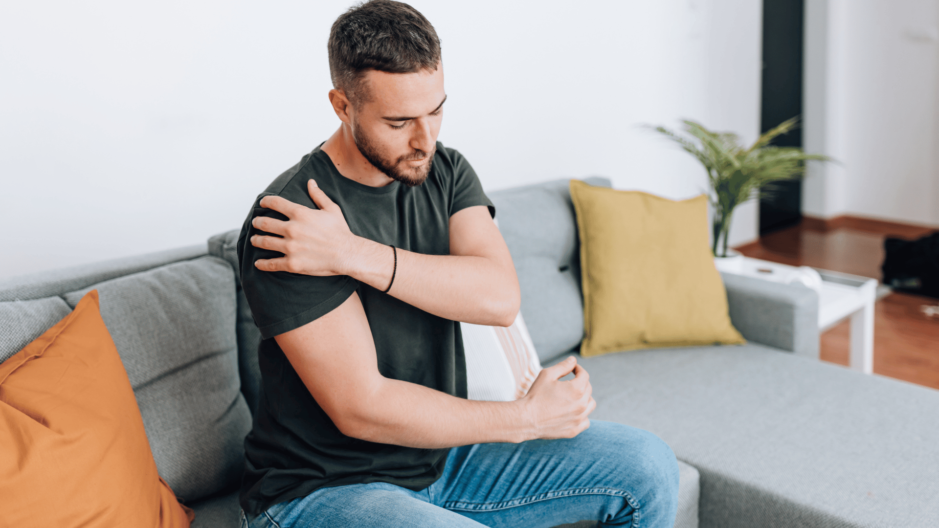 Schulter ausgekugelt Titelbild - Mann sitzt auf dem Sofa und hält sich mit schmerzverzerrtem Gesicht die Schulter, offenbar wegen Beschwerden im Schulterbereich.