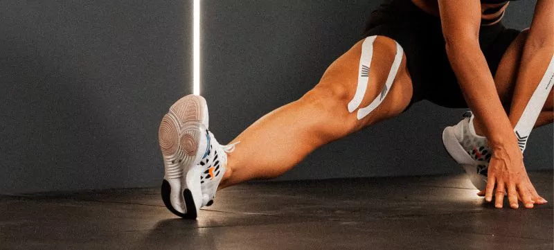 Fuß tapen Titelbild. Athlet führt Dehnübung mit Kinesiologie Tapes an Oberschenkel und Unterschenkel aus – Fokus auf Beinmuskulatur und sportliche Aktivität.