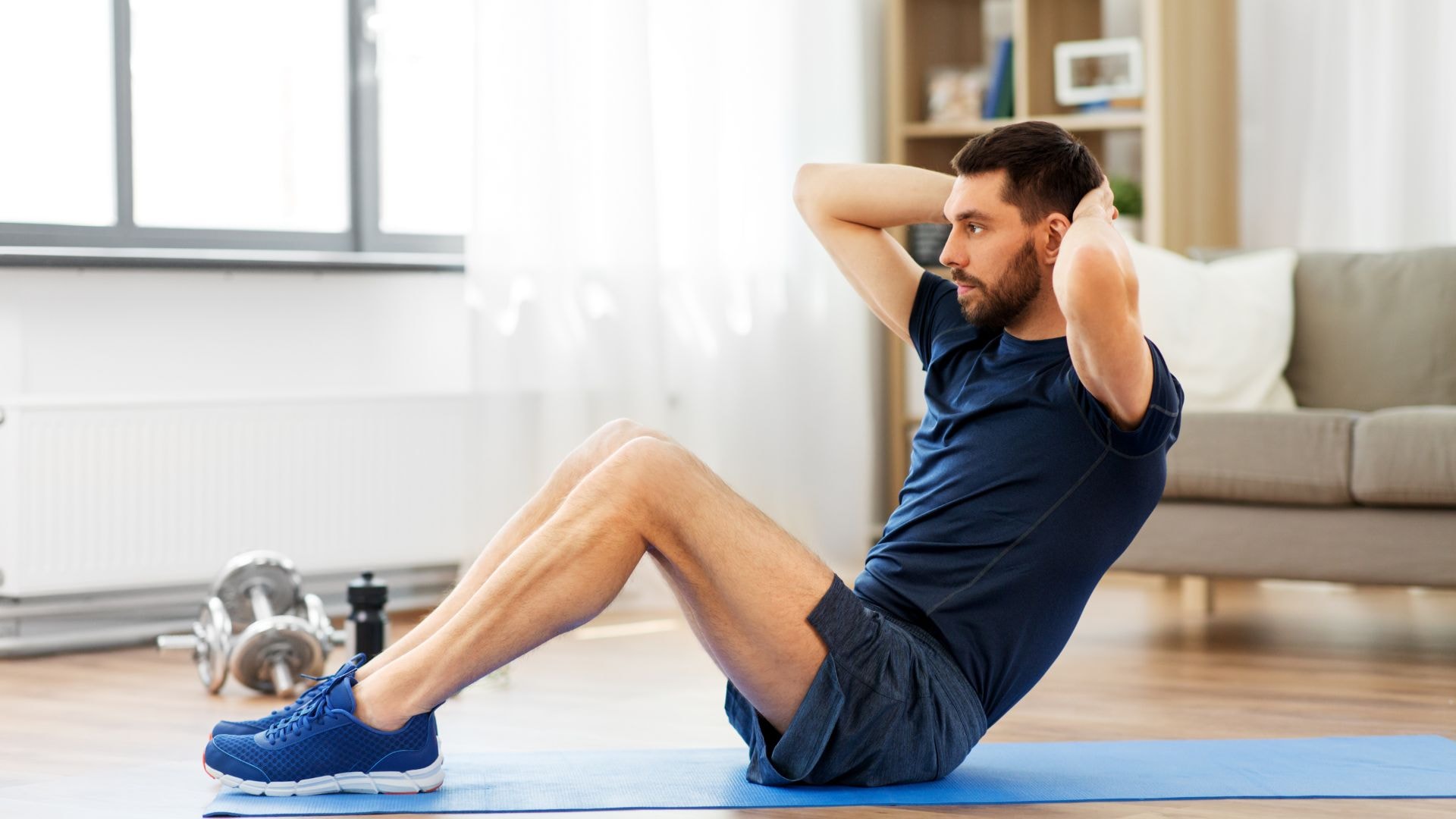 Bauchmuskeltraining Titelbild. Mann macht Sit-ups auf Yogamatte im Wohnzimmer – klassisches Bauchmuskeltraining für zuhause
