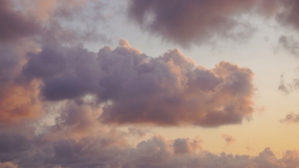 Fluffy clouds drift across a pastel sunset sky