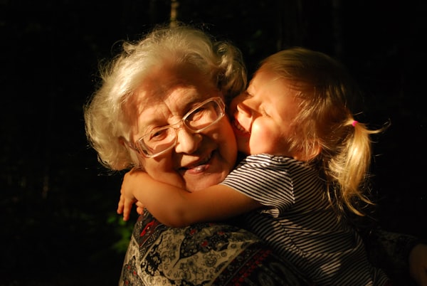 An elderly woman with white hair and glasses hugging a young child