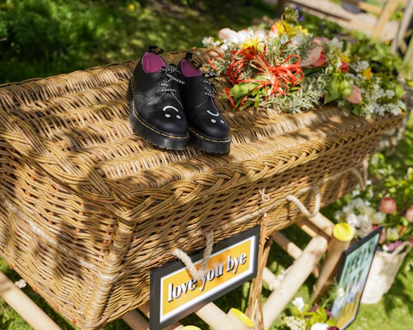 A wicker coffin adorned with black shoes and colorful flowers