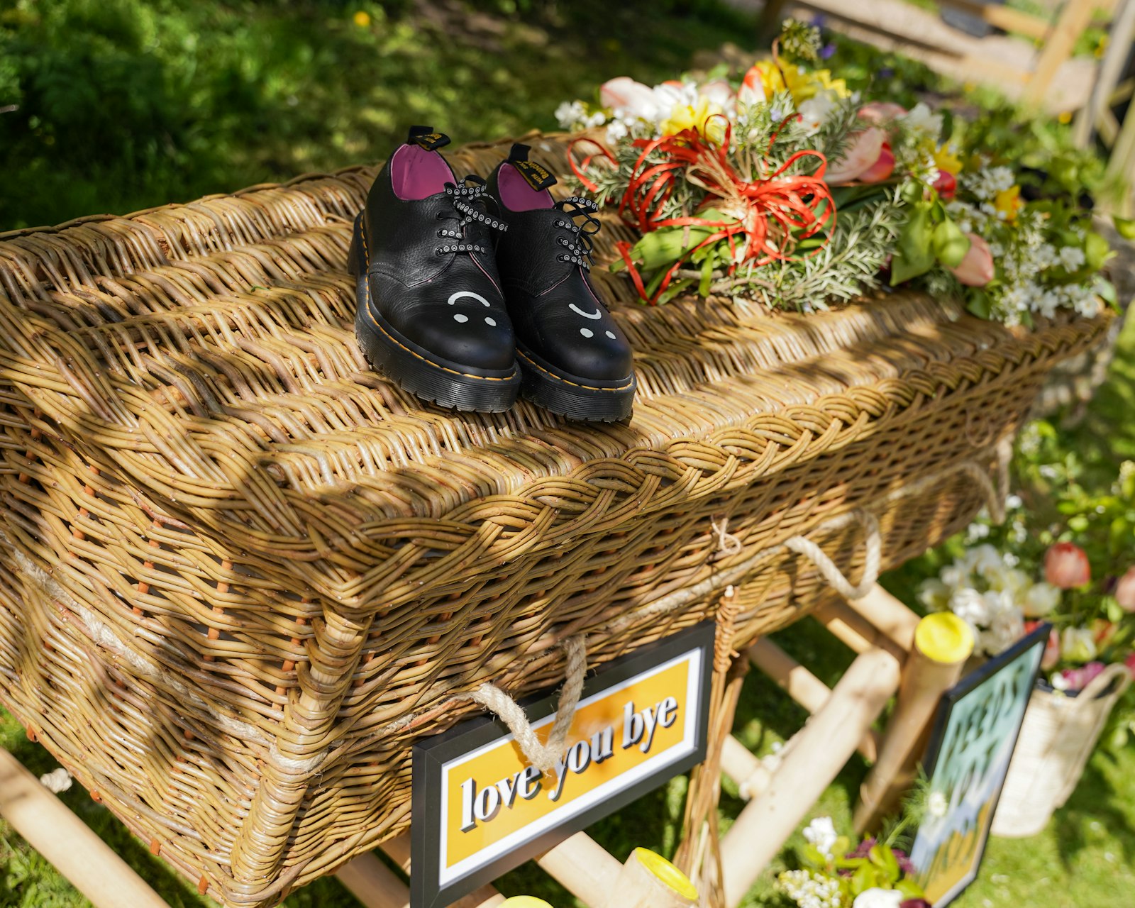A wicker coffin adorned with black shoes and colorful flowers