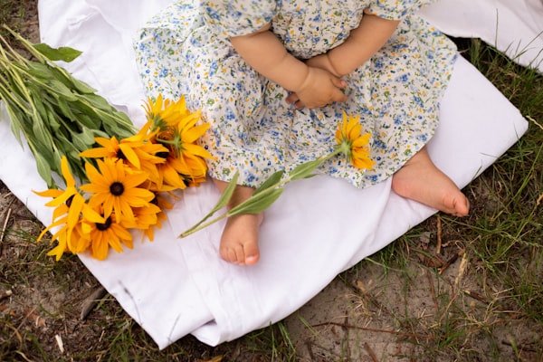 a little girl sitting on a blanket next to a bunch of flowers