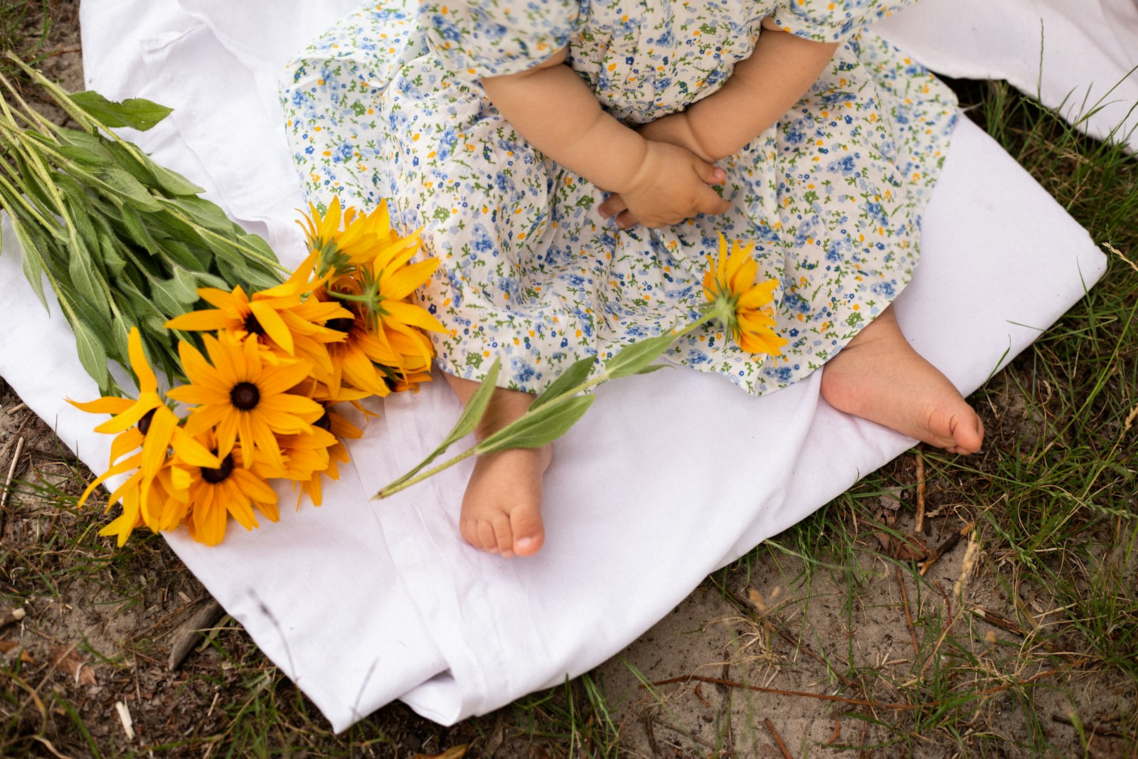a little girl sitting on a blanket next to a bunch of flowers